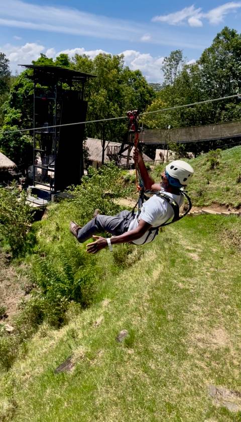 Man zip-lining over green vegetation wearing helmet and harness.