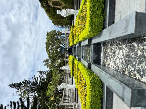 Symmetrical garden with stone water channel and manicured yellow hedges lined by statues.