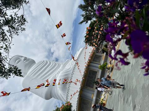 Giant seated Buddha statue with festive prayer flags and visitors walking below.