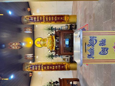 Indoor Buddhist shrine with golden statue, offering table and decorative columns.