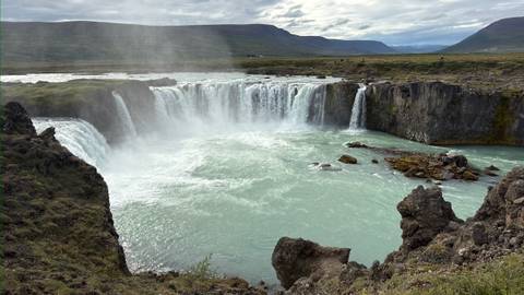 Powerful waterfall cascading into a turquoise pool surrounded by rugged cliffs and mist.