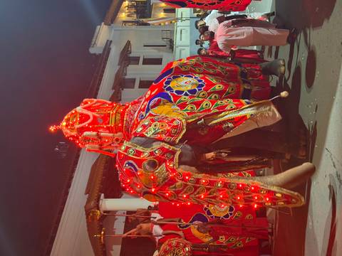 Brilliantly lit and decorated elephant leads a night-time cultural parade with attendants in traditional dress.