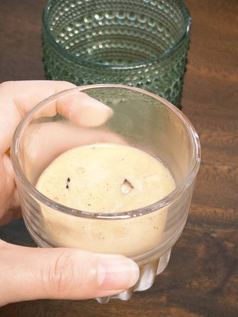 Hand holding a glass of frothy egg coffee viewed from above.