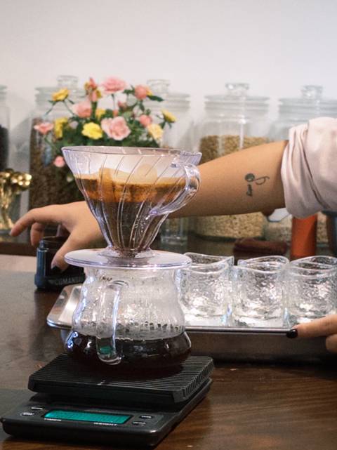 Barista hand using a V60 pour-over dripper above a glass jug during a coffee workshop.