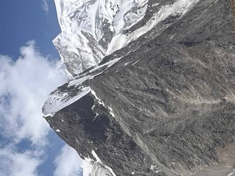 Sharp, jagged snow-capped peak rising into a blue sky with wisps of cloud.