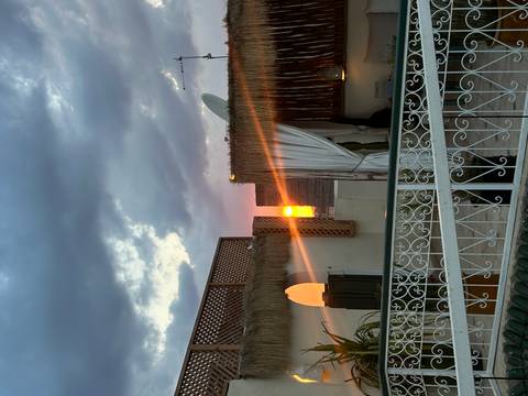 Sunset glow peeking between rooftops of a riad terrace adorned with latticework and curtains.