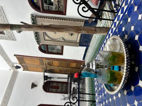 Traditional Moroccan mint tea set on a tiled courtyard table beside an ornate fountain and carved wood doors.