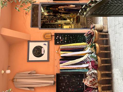 Market stall displaying colorful scarves and textiles against a warm terracotta wall.