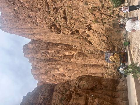 Vehicles and visitors dwarfed by towering reddish canyon walls in a dramatic gorge.