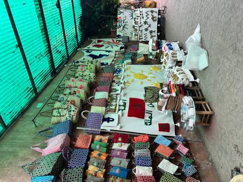 Outdoor stall selling woven bags and embroidered textiles beneath a green corrugated roof.