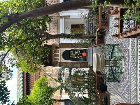 Beautifully tiled riad courtyard with central fountain framed by orange trees and intricate Moorish doorways.