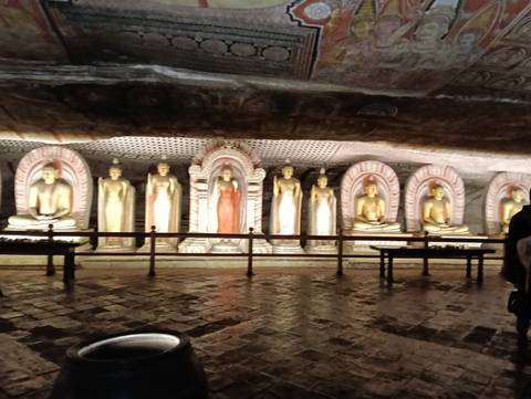 Dimly lit interior of Dambulla Cave Temple lined with golden seated and standing Buddha statues.