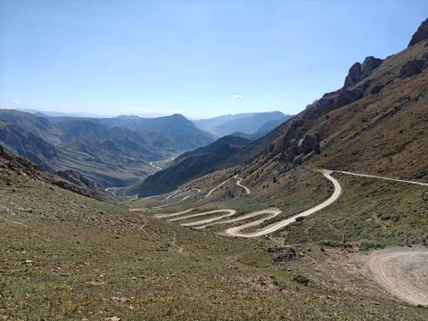 High mountain panorama with a serpentine road snaking through valleys toward hazy distant peaks.