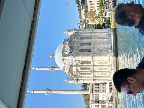 Ortaköy Mosque gleams in the sun beside the Bosphorus, framed by ferry passengers.