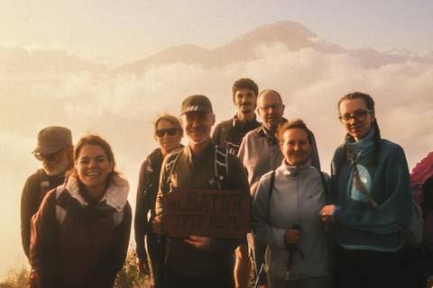 Hikers pose with a wooden Mt. Batur summit sign amid misty sunrise clouds.