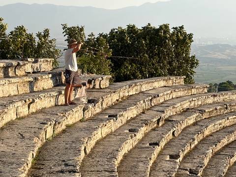 Traveler playfully aiming a mock spear from the stone seating of an ancient Roman amphitheater.