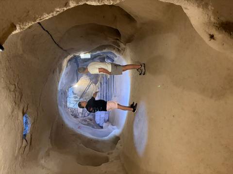 Guide explaining rock-hewn passages inside an underground city while two visitors listen.