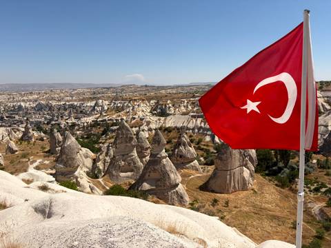 Turkish flag fluttering above Cappadocia’s distinctive fairy-chimney landscape under clear skies.