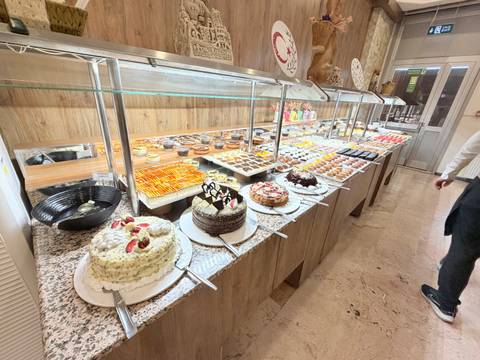 Extensive hotel dessert buffet with rows of cakes, pastries and sweets under glass sneeze guards.