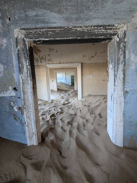 Sand-filled abandoned house with successive door frames creating a striking perspective in Kolmanskop.