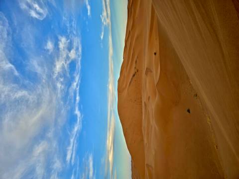 Vast orange dunes under blue sky streaked with wispy clouds at dusk.
