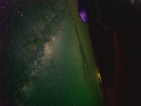 Star-filled sky above silhouetted dunes with faint glow of distant lights on horizon.