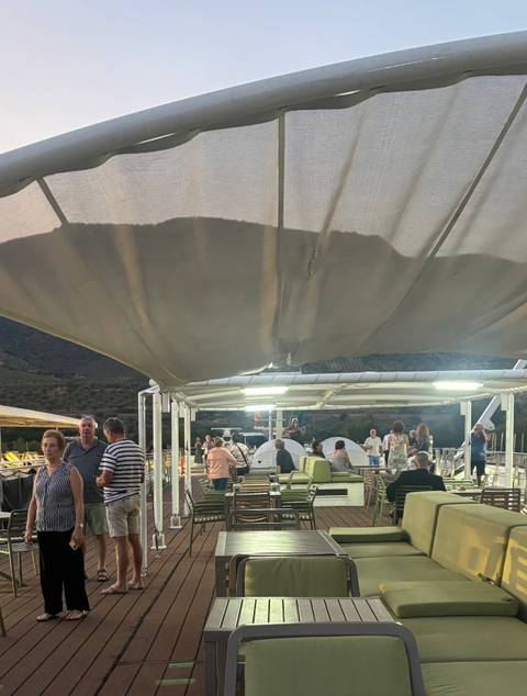 Evening gathering of cruise passengers relaxing on a covered sun deck with lounge seating.