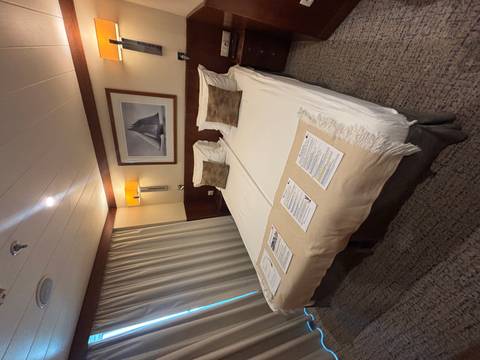 Neat twin-bed cabin with soft lighting, framed sailing photograph and informational leaflets on the beds.