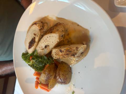 Plated main course of roasted chicken breast with potatoes, vegetables and herb garnish.