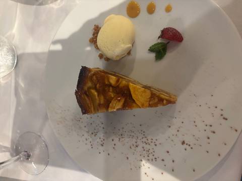 Slice of apple tart served with vanilla ice-cream, strawberry and mint on a white plate.
