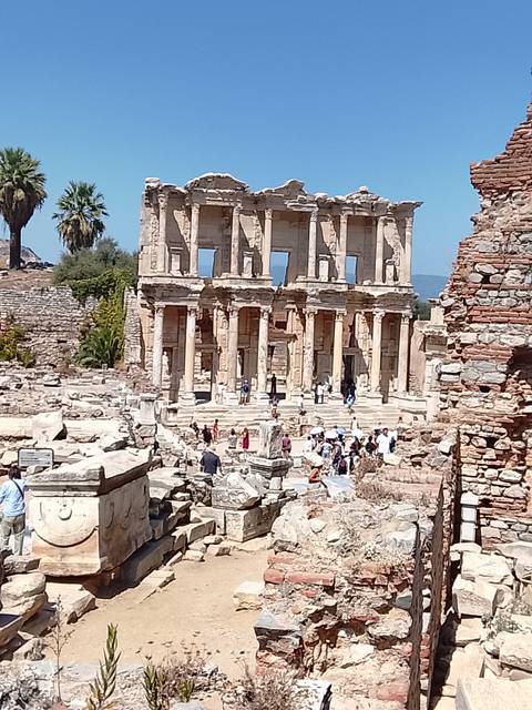 Ancient stone façade of the Library of Celsus with tourists exploring the surrounding ruins.