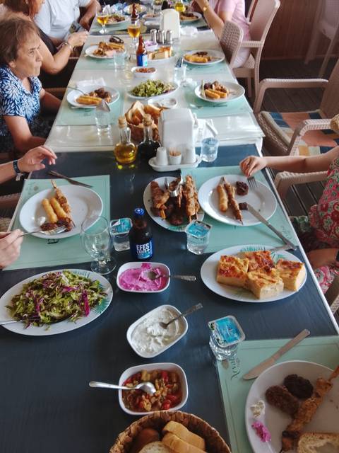 Tabletop view of Turkish meal with skewers, salad, meze and Efes beer as diners reach for food.