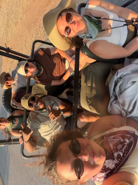 Motion-blurred selfie of travelers aboard an open safari vehicle smiling at the camera.