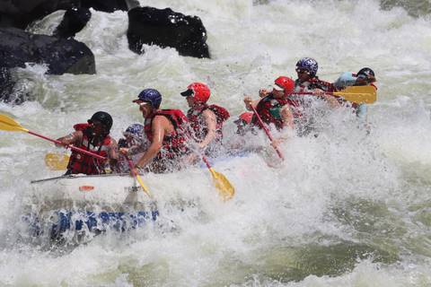 Thrilling white-water rafting team battles through crashing rapids with paddles raised.