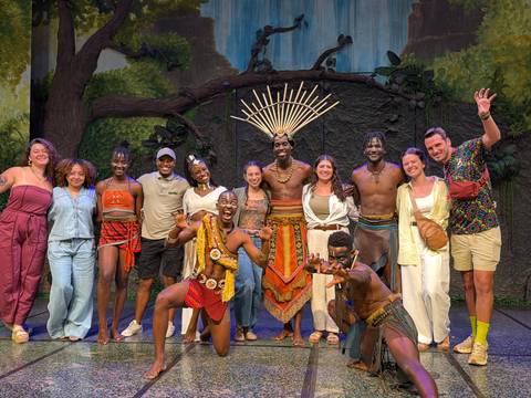 Group photo with energetic cultural performers in vibrant costumes on stage.