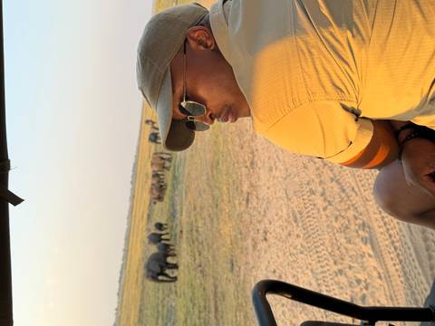 Traveler sits on safari vehicle edge watching a distant herd of elephants on open plain.