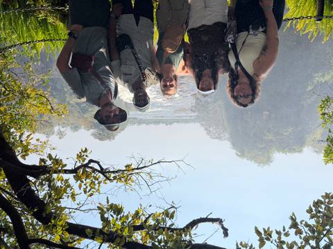 Group of travelers silhouetted against misty waterfall backdrop framed by foliage.