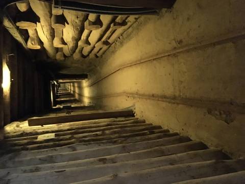 Dimly lit historic mine tunnel with narrow rail tracks stretching into the distance.