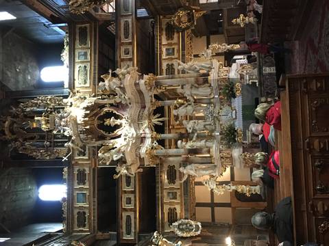 Elaborate baroque altar inside a historic church with visitors seated in pews.