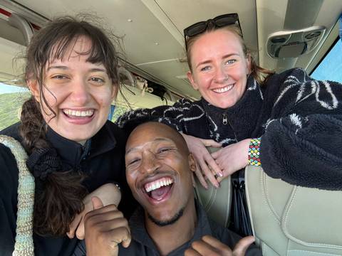 Three friends laugh together inside a vehicle, capturing a joyful selfie.