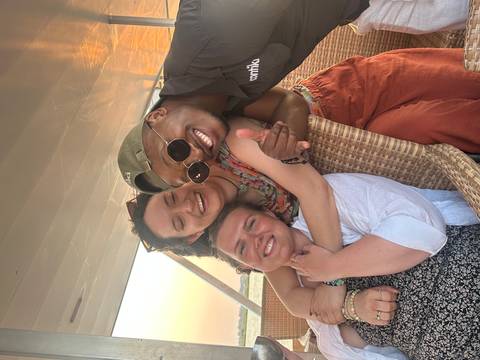 Trio enjoys sunset on a boat, sharing hugs and smiles under warm light.