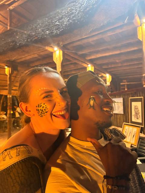 Two friends with painted faces laugh playfully in a warmly lit rustic venue.