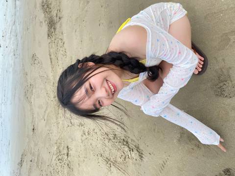 Smiling young woman crouching happily on a sandy beach.
