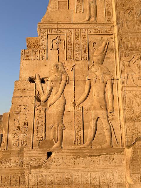 Sunlit sandstone reliefs depicting ancient Egyptian deities and hieroglyphics on a temple wall.