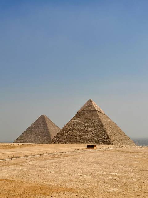 Two iconic pyramids rising from the desert against a pale blue sky.