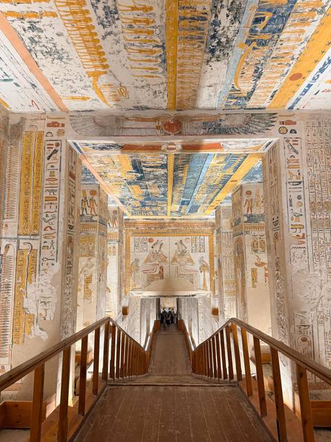 Vibrantly painted corridor ceiling and walls filled with hieroglyphs and ancient figures inside a royal tomb.