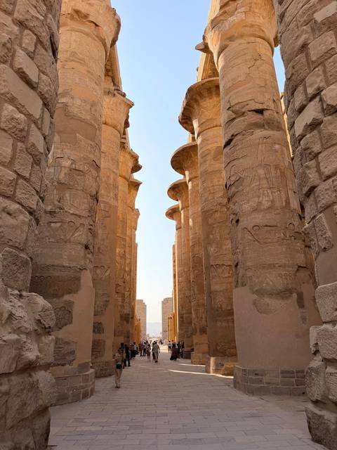 Massive sandstone columns adorned with carvings form a corridor in an ancient Egyptian temple.