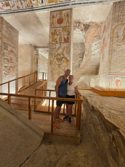 Travelers stand inside an ancient Egyptian temple hallway adorned with colorful reliefs and wooden walkways.