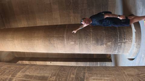 Visitor points to intricate hieroglyphs carved on a massive stone column inside an Egyptian temple.
