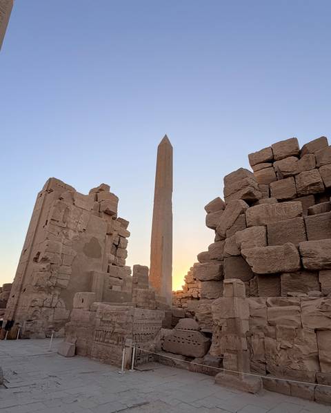 Tall ancient obelisk framed by massive sandstone blocks glows against a pastel evening sky.